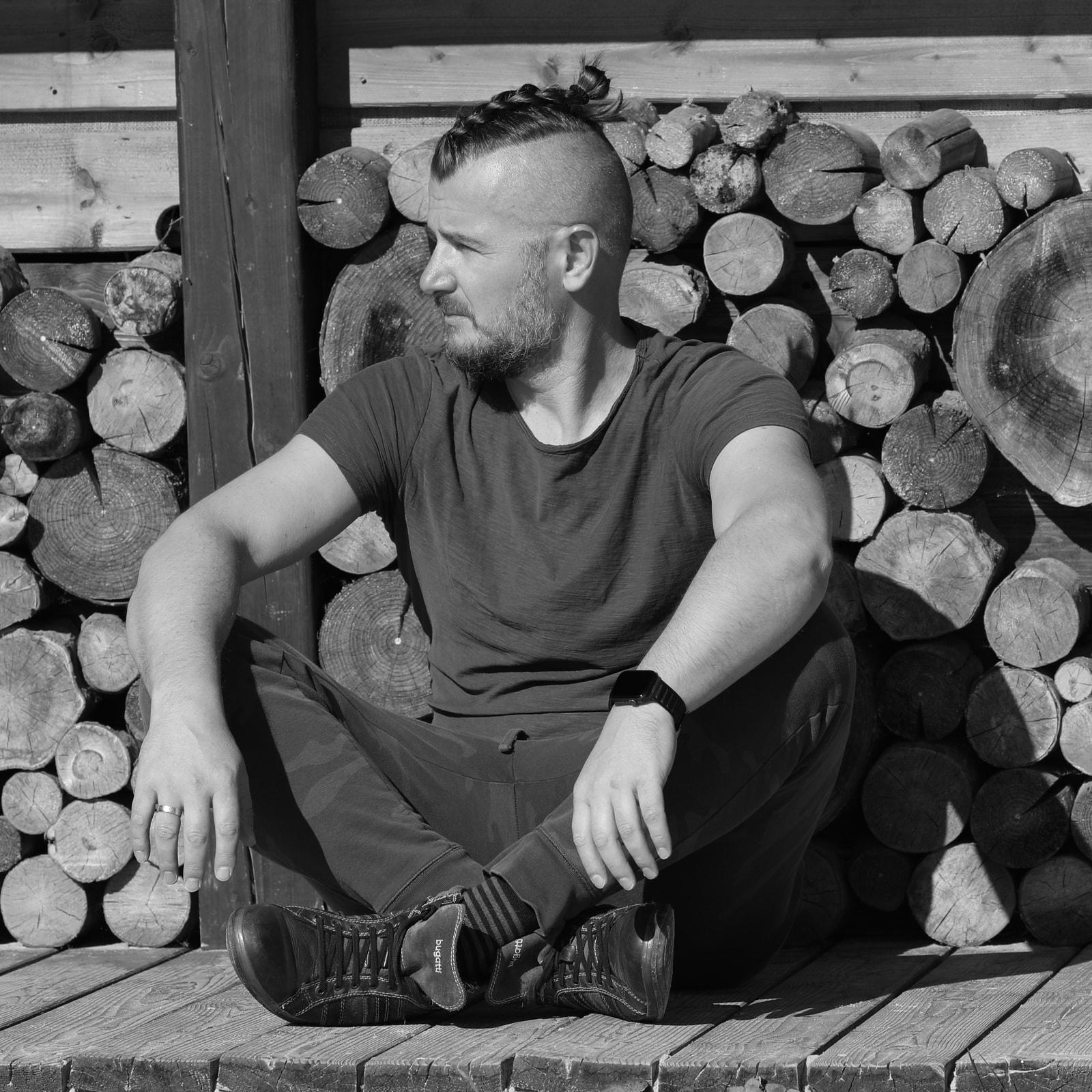 Svart-hvitt portrett av fotografen ved en vedstabel